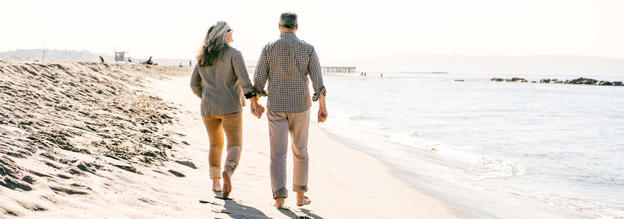 a retired couple walking down the beach on a sunny day