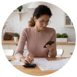 a woman wearing light pink calculating her income and expenses on the kitchen table